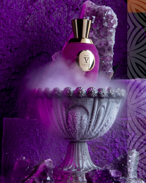 Flakon perfum V Canto Alki w intensywnie fioletowej oprawie, ustawiony na ozdobnym kamiennym kielichu otoczonym mgłą, z kryształami w tle. Luksusowy, elegancki design z złotym korkiem i emblematem, podkreślony mistyczną, alchemiczną atmosferą