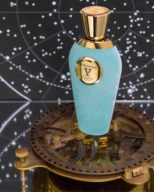 Flakon perfum V Canto Astronomo w turkusowym, welurowym wykończeniu ze złotymi detalami, stojący na mosiężnym astrolabium, na tle mapy gwiazd