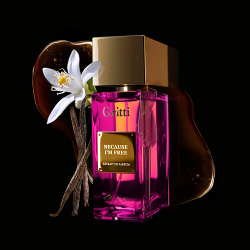 Flakon perfum Gritti Because I’m Free w intensywnie różowym kolorze z złotą nakrętką i etykietą. Obok butelki znajdują się kwiat jaśminu oraz laska wanilii na ciemnym tle, podkreślając luksusowy i zmysłowy charakter zapachu