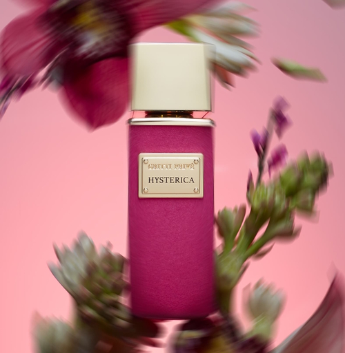 Flakon perfum Gritti Hysterica z kolekcji Privé – elegancka butelka w różowym welurowym wykończeniu z pozłacaną tabliczką i kremowym korkiem, otoczona rozmytymi kwiatami na różowym tle