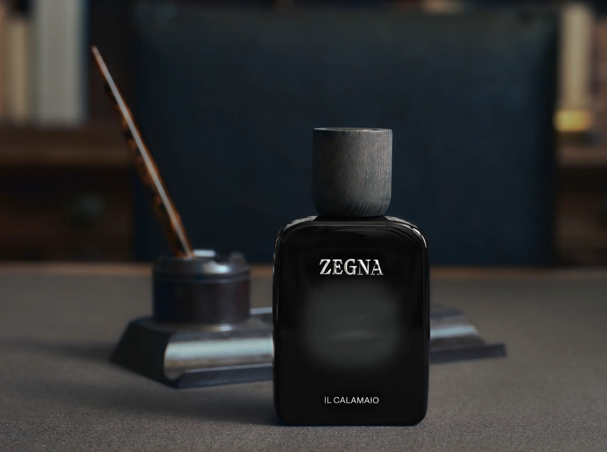 Flakon perfum Zegna Il Calamaio na tle inspirowanym biurkiem, atramentem i papierem. Kompozycja podkreśla elegancki, skórzano-ambrowy charakter zapachu.