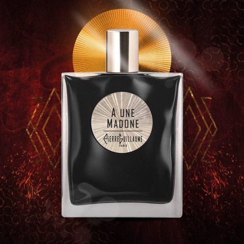 Czarny flakon perfum **A Une Madone Pierre Guillaume Paris** o minimalistycznym, eleganckim kształcie, z jasnym cylindrycznym korkiem. Na froncie butelki znajduje się okrągła etykieta w odcieniach srebra z nazwą zapachu. Flakon ustawiony jest na tle ciemnej, głębokiej czerwieni z abstrakcyjnymi, złotymi geometrycznymi motywami i świetlistą aurą, podkreślającą zmysłowy, mistyczny i luksusowy charakter zapachu.