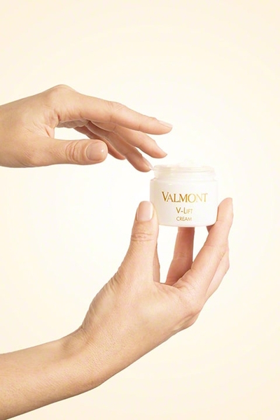Słoiczek kremu Valmont V-Lift Cream trzymany w dłoniach na jasnym, neutralnym tle. Minimalistyczne, eleganckie opakowanie podkreśla luksusowy charakter liftingującego kremu do twarzy z linii V-Lift